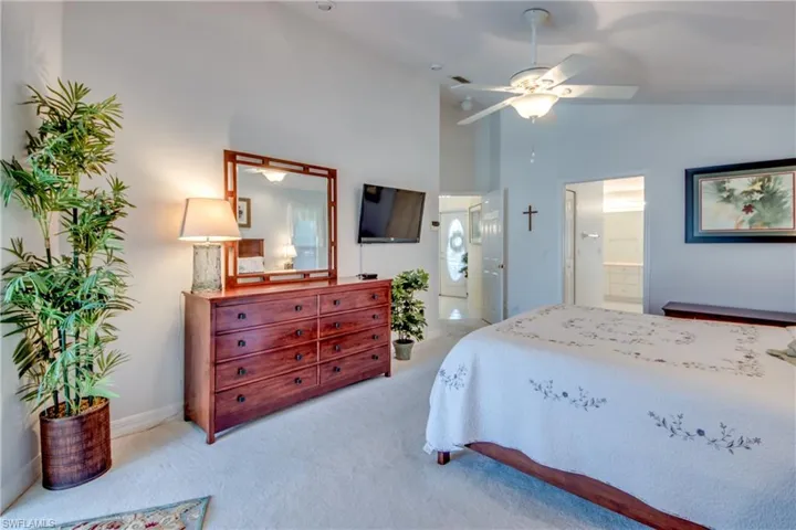 Bedroom featuring light carpet, connected bathroom, high vaulted ceiling, and ceiling fan