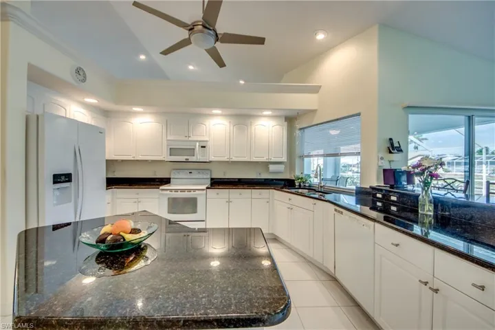 Kitchen featuring sink, white cabinetry, light tile patterned floors, dark stone countertops, and white appliances
