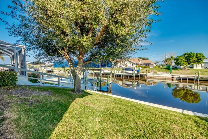 View of dock featuring a lanai, a lawn, and a water view