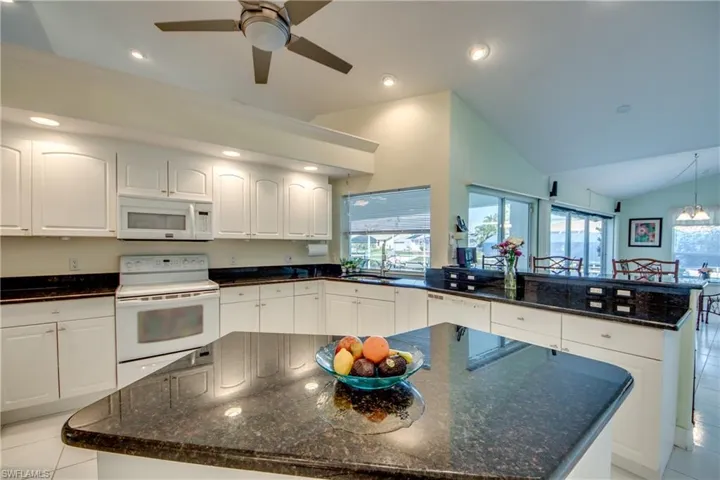 Kitchen featuring white cabinetry, white appliances, a kitchen island, and dark stone countertops