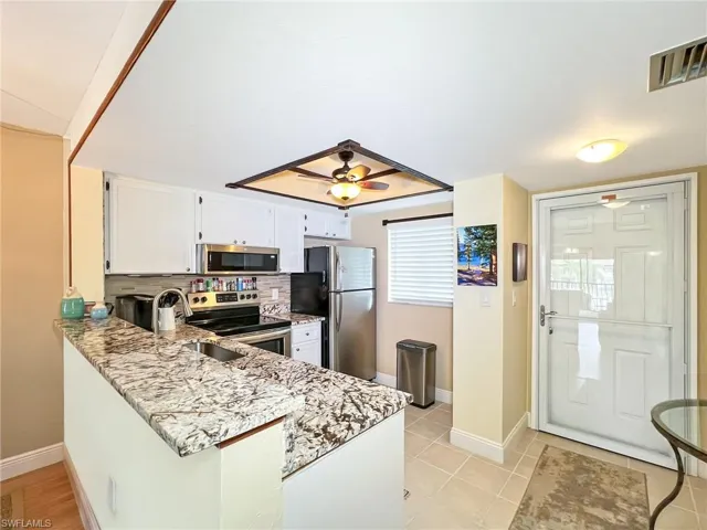 Kitchen featuring sink, light tile patterned floors, light stone countertops, appliances with stainless steel finishes, and white cabinetry