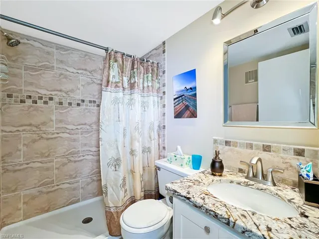 Bathroom with backsplash, curtained shower, vanity, and toilet