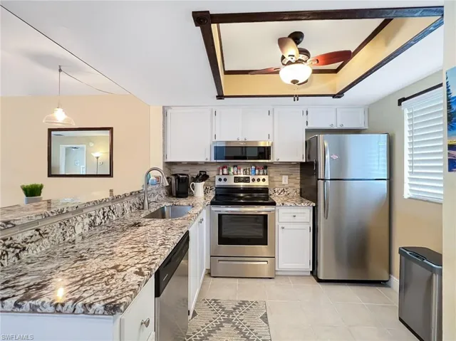 Kitchen with light stone countertops, sink, white cabinetry, and stainless steel appliances