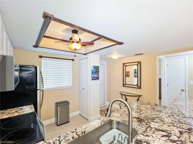 Kitchen featuring stove, ceiling fan, light stone countertops, light tile patterned floors, and fridge