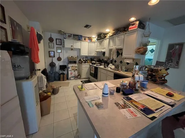 Kitchen featuring stainless steel microwave, light tile patterned floors, electric stove, white cabinets, and a peninsula