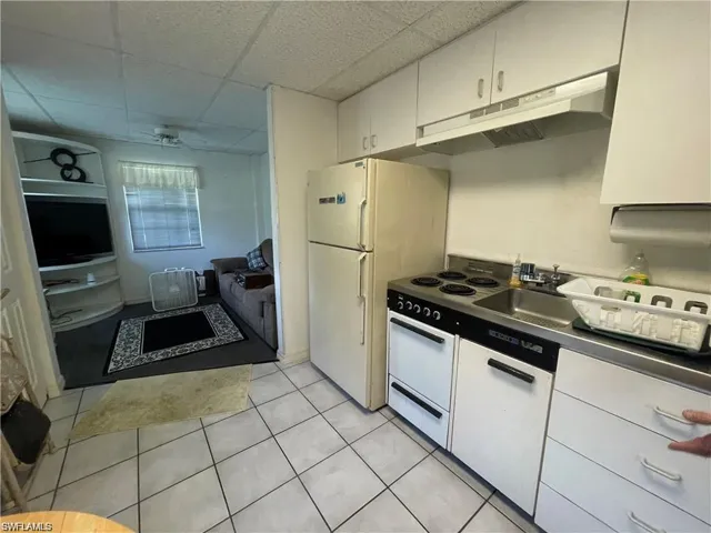 Kitchen with under cabinet range hood, a drop ceiling, a sink, light tile patterned flooring, and white cabinets