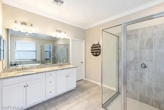 Full bathroom featuring a shower stall, double vanity, ornamental molding, and light tile patterned flooring