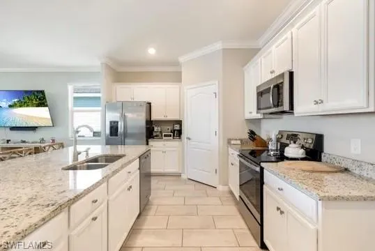 Kitchen featuring stainless steel appliances, white cabinets, crown molding, light stone countertops, and recessed lighting