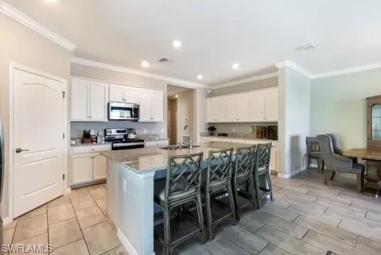 Kitchen with a breakfast bar, white cabinets, stainless steel appliances, a center island with sink, and crown molding