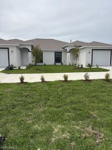 View of front of house featuring a garage, concrete driveway, a front lawn, and stucco siding