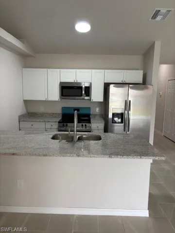Kitchen with stainless steel appliances, white cabinets, light stone counters, and light tile patterned floors