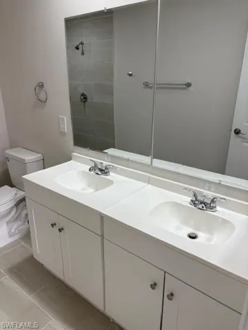 Bathroom featuring double vanity, tiled shower, and light tile patterned flooring