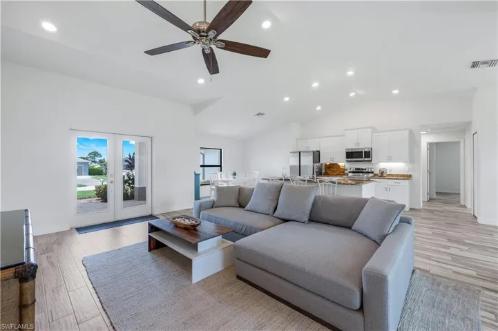 Spacious open great room with recessed lighting, wood look tile, ceiling fan, volume ceilings, and glass front doors.