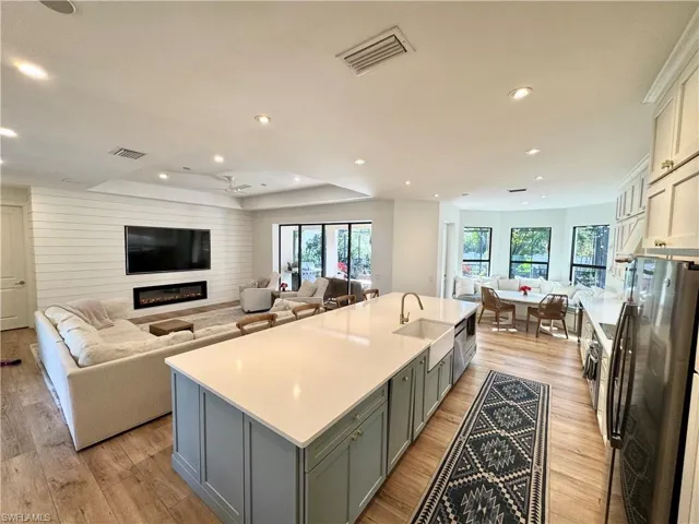 Kitchen featuring visible vents, open floor plan, a kitchen island with sink, light countertops, and a sink