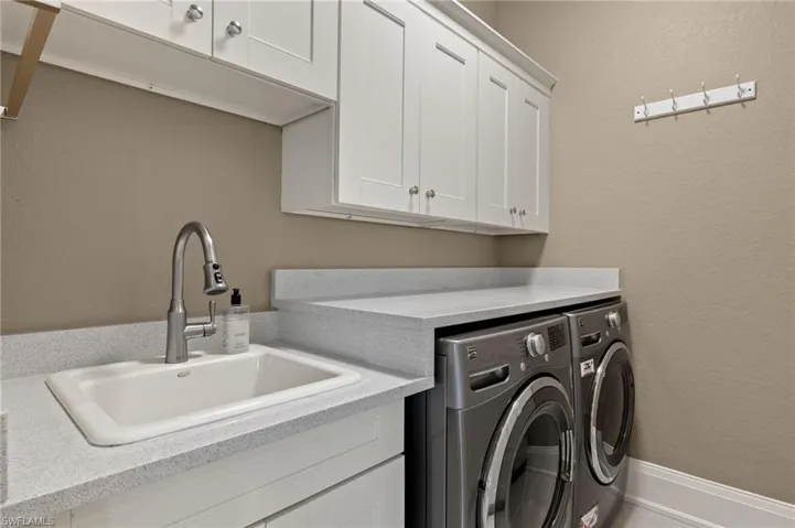 Clothes washing area featuring washing machine and clothes dryer, cabinets, and sink