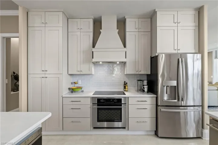 Kitchen with white cabinetry, appliances with stainless steel finishes, backsplash, custom exhaust hood, and crown molding