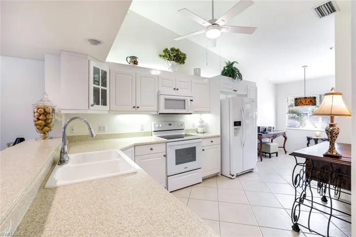 Kitchen with lofted ceiling, white appliances, white cabinetry, a ceiling fan, and light tile patterned flooring