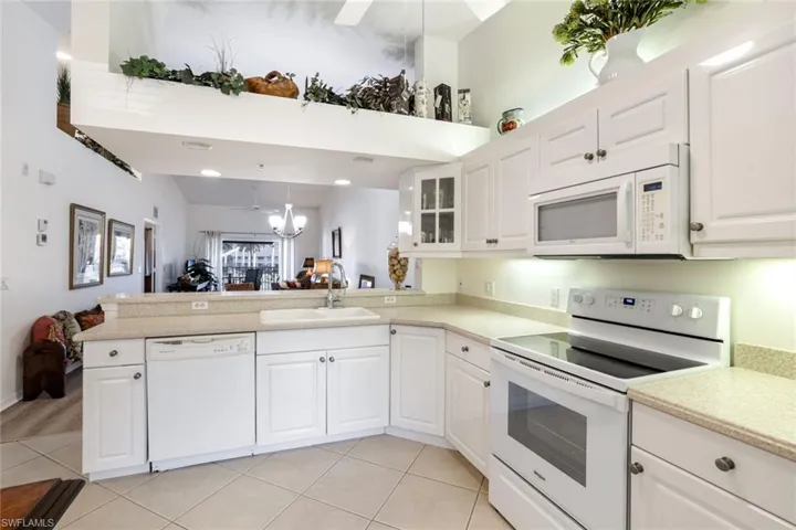 Kitchen with white appliances, a peninsula, glass insert cabinets, white cabinetry, and decorative light fixtures