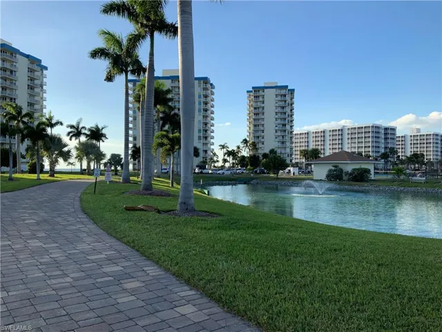 Pond with fountain along driveway lined with tall palms line trees.