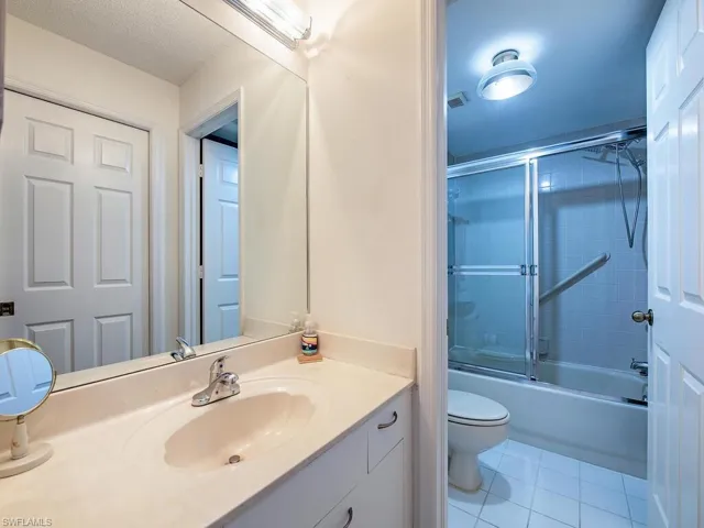 Bathroom with tile patterned flooring, toilet, vanity, and bath / shower combo with glass door