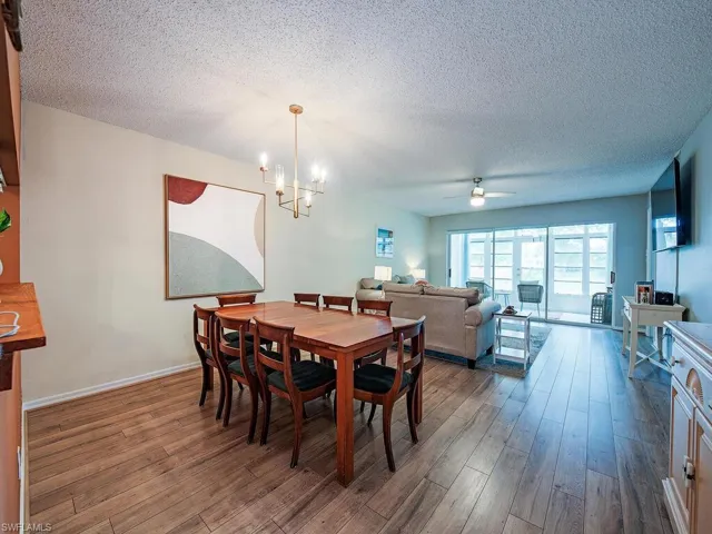 Dining area with a chandelier, wood finished floors, a textured ceiling, a ceiling fan, and baseboards