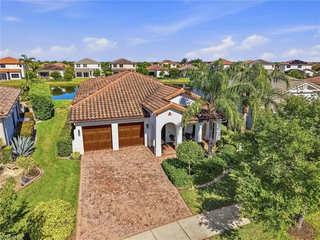 This property features a terracotta tile roof, a two-car garage with wooden doors, and a paver driveway