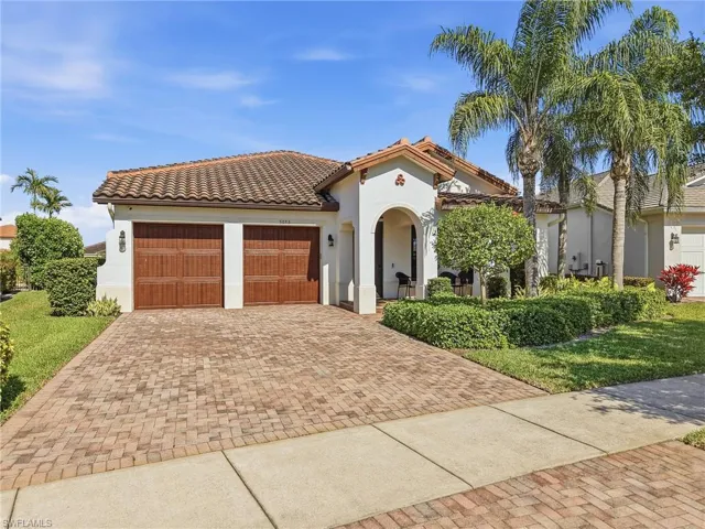 The property features a Mediterranean-style exterior with a tiled roof, a two-car garage with wood-paneled doors, and a paver driveway