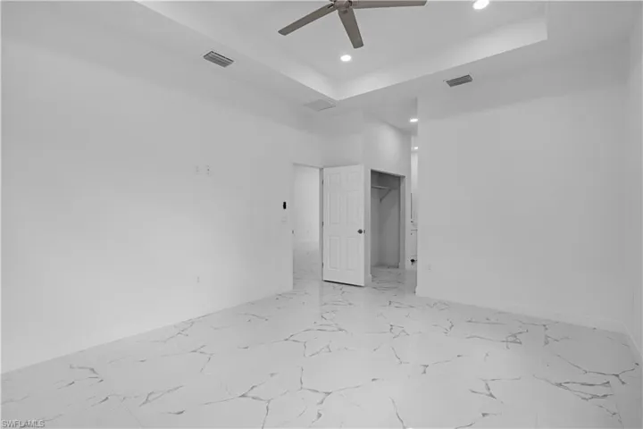 Unfurnished bedroom with a tray ceiling, recessed lighting, a walk in closet, light marble finish flooring, and a ceiling fan