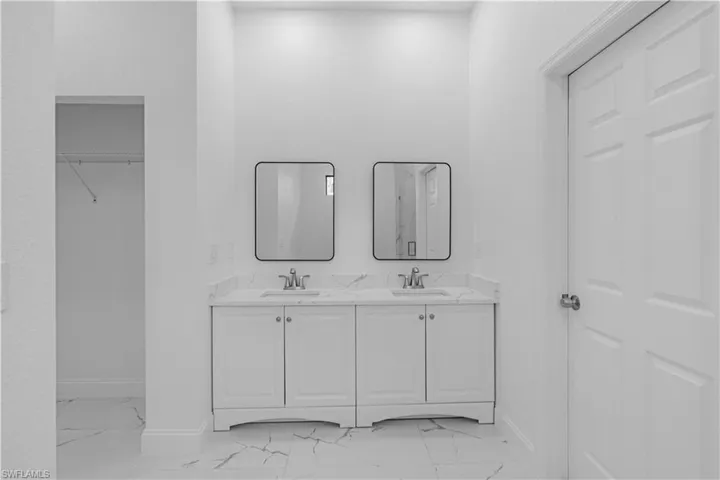 Full bath featuring double vanity, light marble finish flooring, and a walk in closet