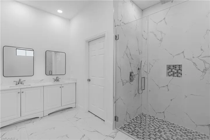 Bathroom with double vanity, a marble finish shower, light marble finish flooring, and recessed lighting