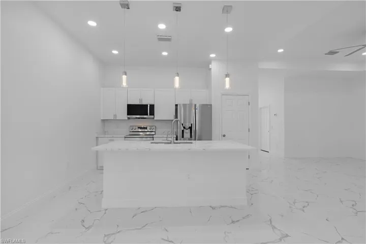 Kitchen featuring decorative light fixtures, appliances with stainless steel finishes, an island with sink, light stone countertops, and recessed lighting