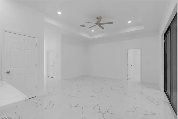 Empty room with a tray ceiling, recessed lighting, light marble finish floors, and ceiling fan