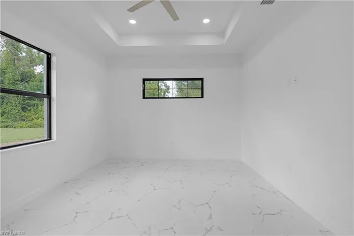 Unfurnished room with light marble finish floors, recessed lighting, ceiling fan, and a raised ceiling