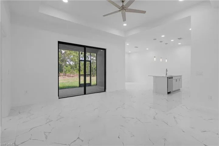 Empty room with a raised ceiling, recessed lighting, light marble finish floors, and a ceiling fan