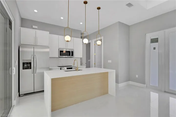 Kitchen featuring appliances with stainless steel finishes, pendant lighting, light stone countertops, white cabinets, and backsplash