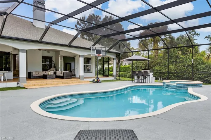 View of pool featuring glass enclosure, an outdoor hangout area, a patio area, and a pool with connected hot tub