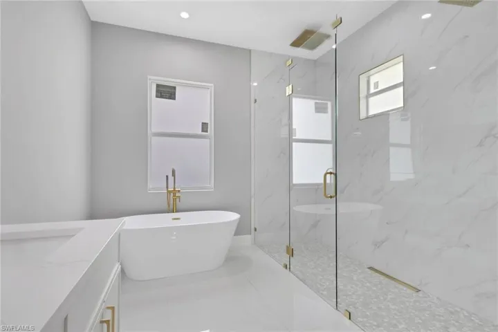 Bathroom featuring vanity, a marble finish shower, a soaking tub, and recessed lighting