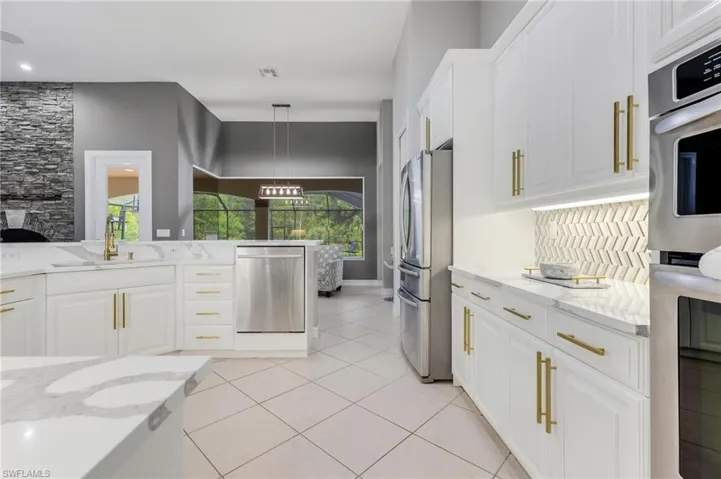 Kitchen with stainless steel appliances, light stone countertops, white cabinetry, hanging light fixtures, and light tile patterned flooring