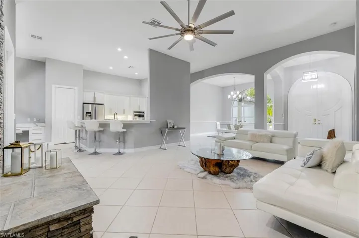 Living room featuring arched walkways, ceiling fan, a chandelier, light tile patterned floors, and recessed lighting