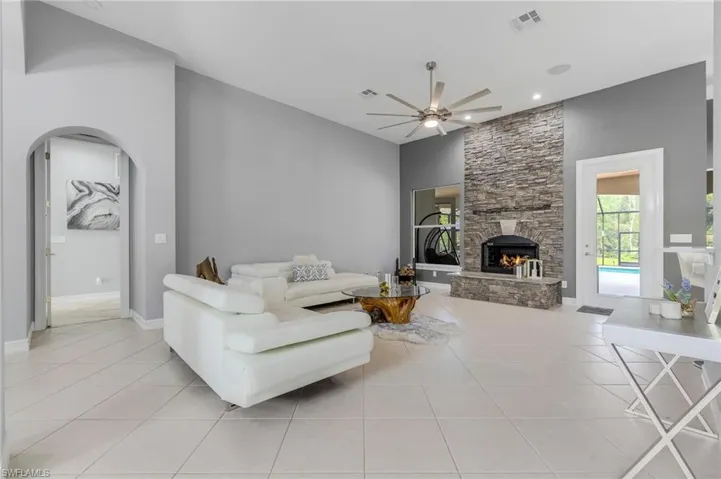 Living area featuring a stone fireplace, light tile patterned flooring, arched walkways, and a ceiling fan