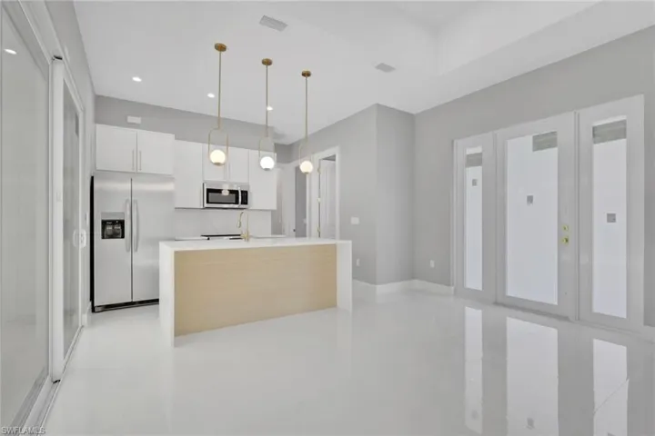 Kitchen with white cabinetry, appliances with stainless steel finishes, hanging light fixtures, a center island with sink, and modern cabinets