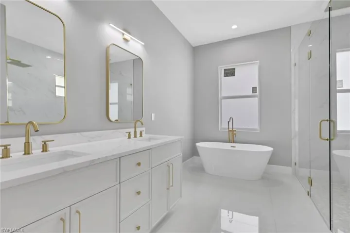Full bath featuring a marble finish shower, a freestanding tub, healthy amount of natural light, double vanity, and recessed lighting