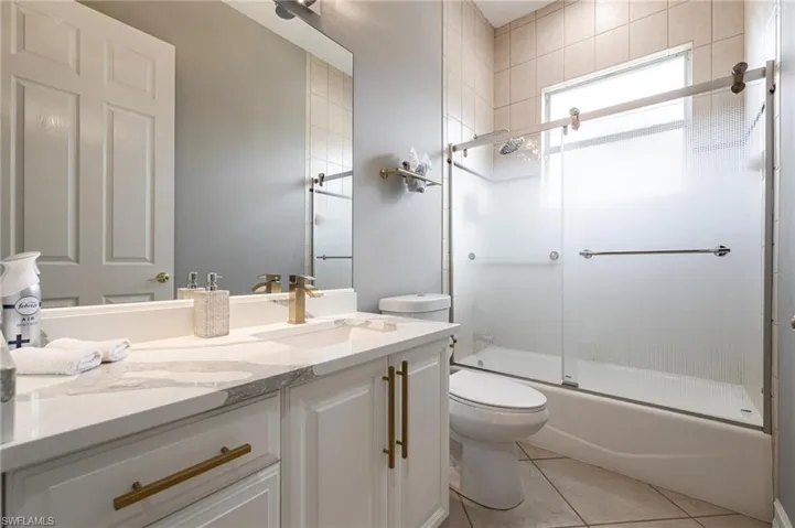 Bathroom featuring vanity, light tile patterned floors, and combined bath / shower with glass door