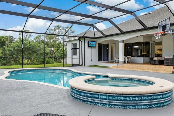 View of swimming pool featuring a sunroom, a patio, a pool with connected hot tub, and glass enclosure