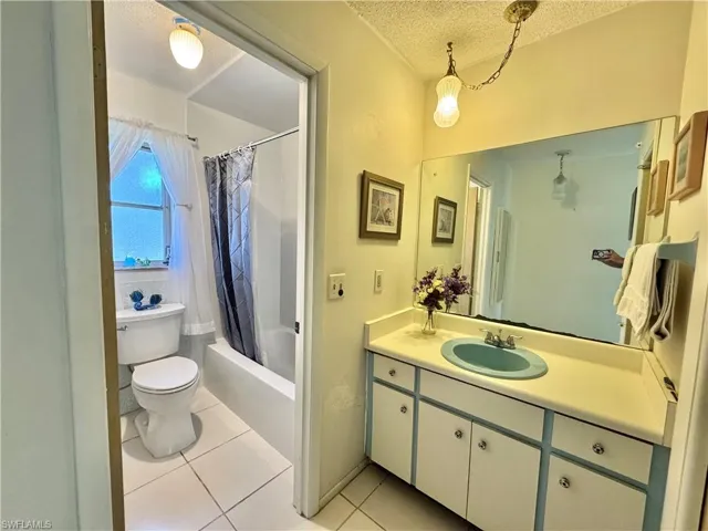 Full bath featuring a textured ceiling, shower / bath combo with shower curtain, vanity, and light tile patterned floors