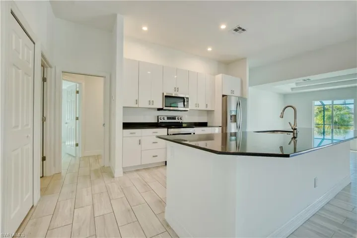 Kitchen featuring a kitchen island with sink, stainless steel appliances, white cabinets, wood finish floors, and recessed lighting