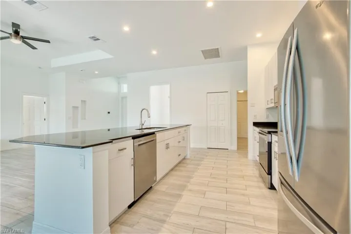 Kitchen with stainless steel appliances, white cabinetry, an island with sink, wood tiled floors, and recessed lighting