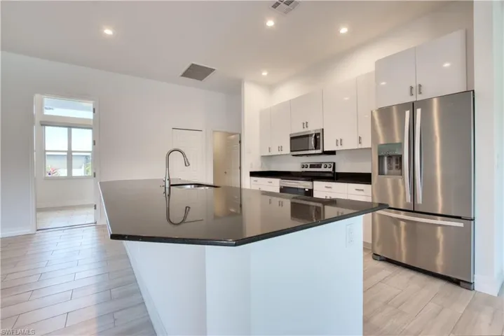Kitchen featuring stainless steel appliances, dark stone counters, white cabinetry, wood tiled floors, and recessed lighting
