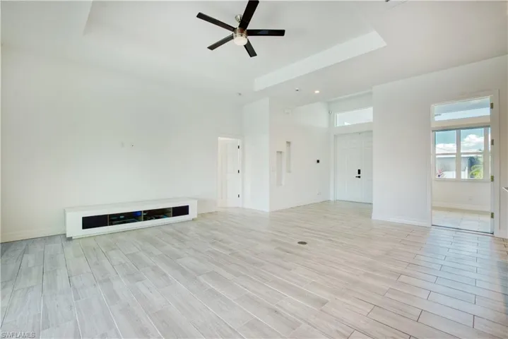 Unfurnished living room with wood tiled floors, ceiling fan, a high tray ceiling, and recessed lighting