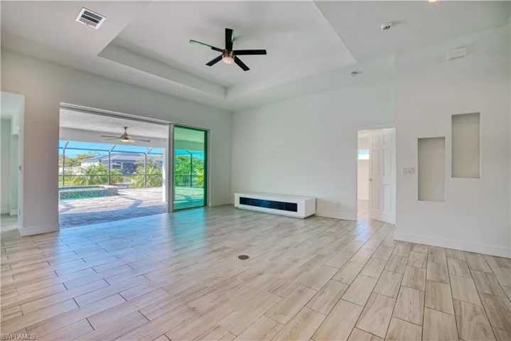 Unfurnished living room with a sunroom, ceiling fan, wood finish floors, and a raised ceiling